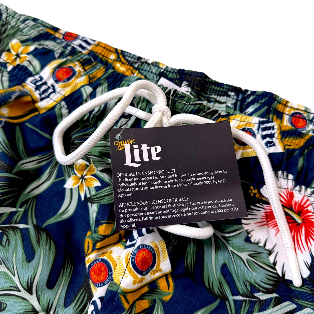 Close-up of a colorful tropical print fabric with white drawstrings and a black hangtag reading 'Miller Lite' and 'Official Licensed Product.'.