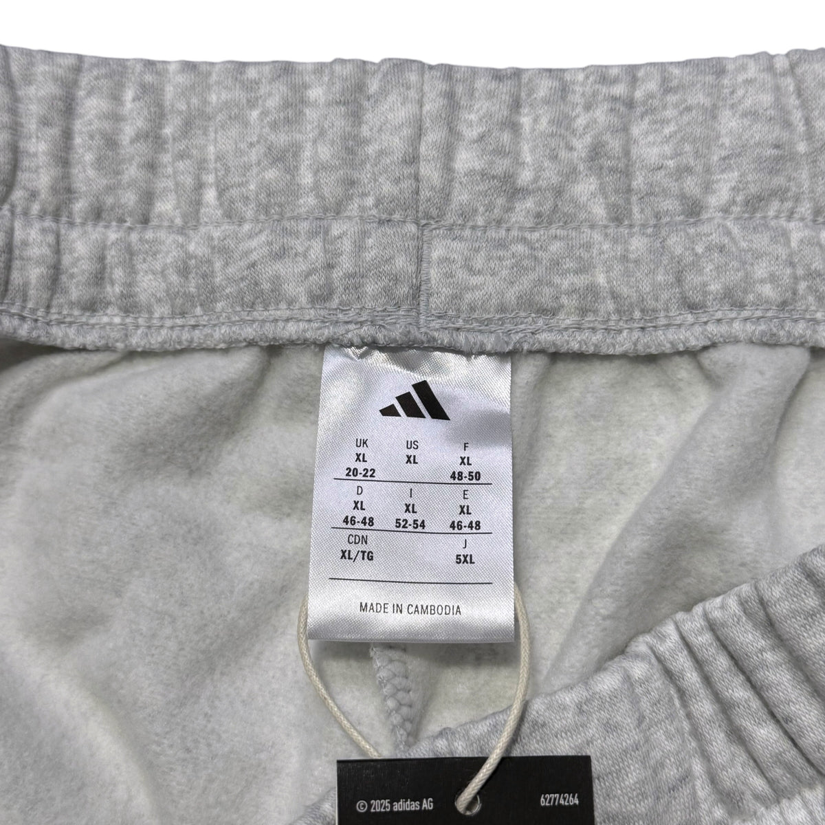 Close-up of the inside waistband of light gray heathered shorts, showing the white Adidas size tag and black hangtag.