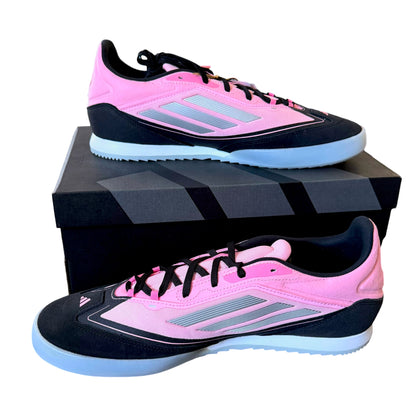 A pair of Adidas soccer shoes in pink and black, displayed on top of and next to their black shoebox against a white background.