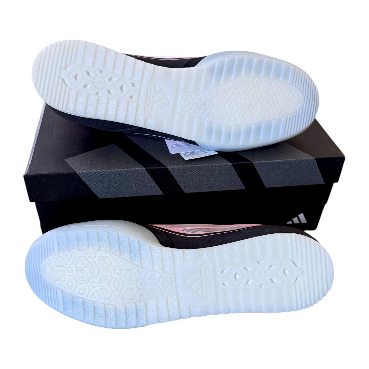 A pair of Adidas sneakers shown from the sole side, stacked on top of a black Adidas shoebox against a white background.