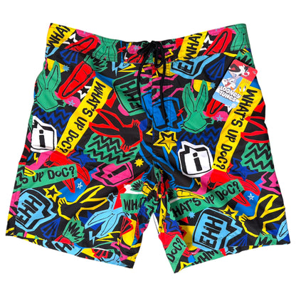 A pair of men's swim trunks featuring a vibrant, multicolor graffiti-style print with the phrase 'WHAT'S UP DOC?' repeated in yellow, black, white, green, blue, and pink. The swim trunks have a black drawstring waistband and are shown flat against a solid white background.