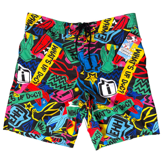 A pair of men's swim trunks featuring a vibrant, multicolor graffiti-style print with the phrase 'WHAT'S UP DOC?' repeated in yellow, black, white, green, blue, and pink. The swim trunks have a black drawstring waistband and are shown flat against a solid white background.