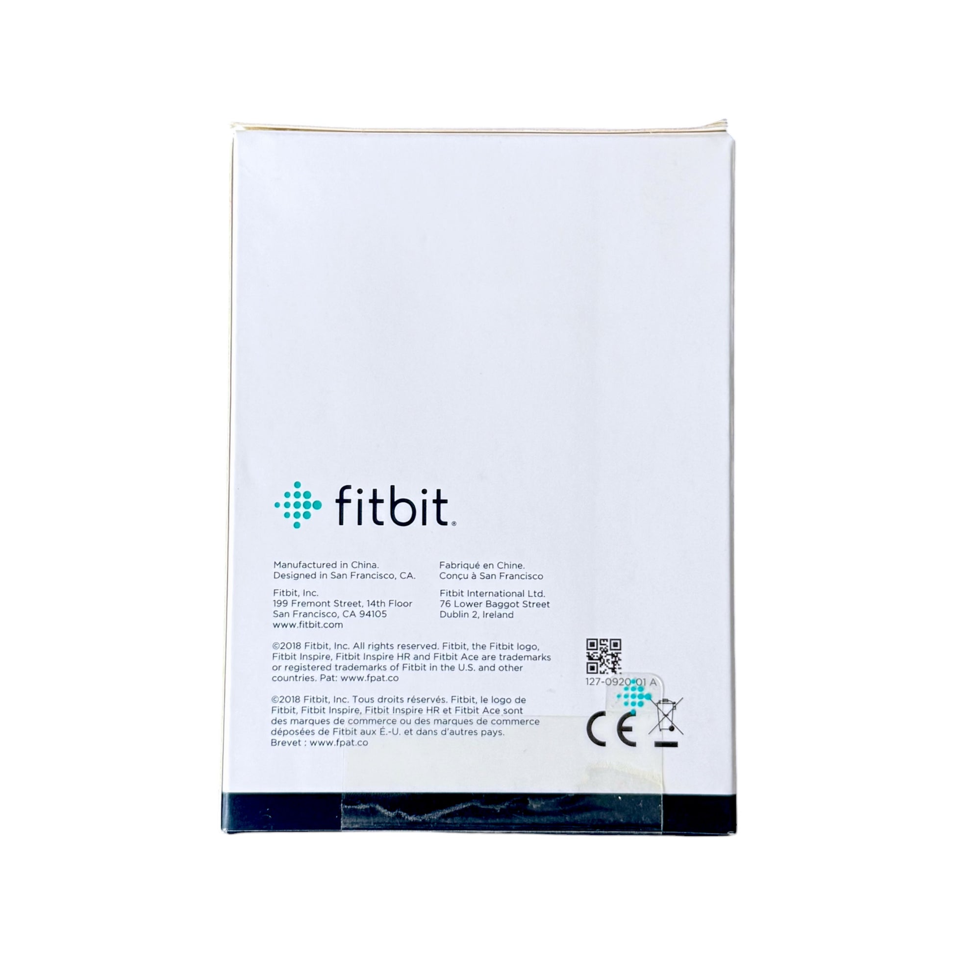 The back of a white Fitbit product box on a plain white background, showing the Fitbit logo, manufacturing details, a QR code, and CE markings.