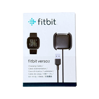 Fitbit Versa 2 charging cable and charging dock in its original white retail packaging, featuring the Fitbit logo and product illustrations.