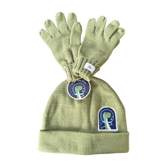 A light sage green knit kids FlapJackKids beanie and glove set, featuring a matching circular hangtag and a small dinosaur patch on the front of the beanie.
