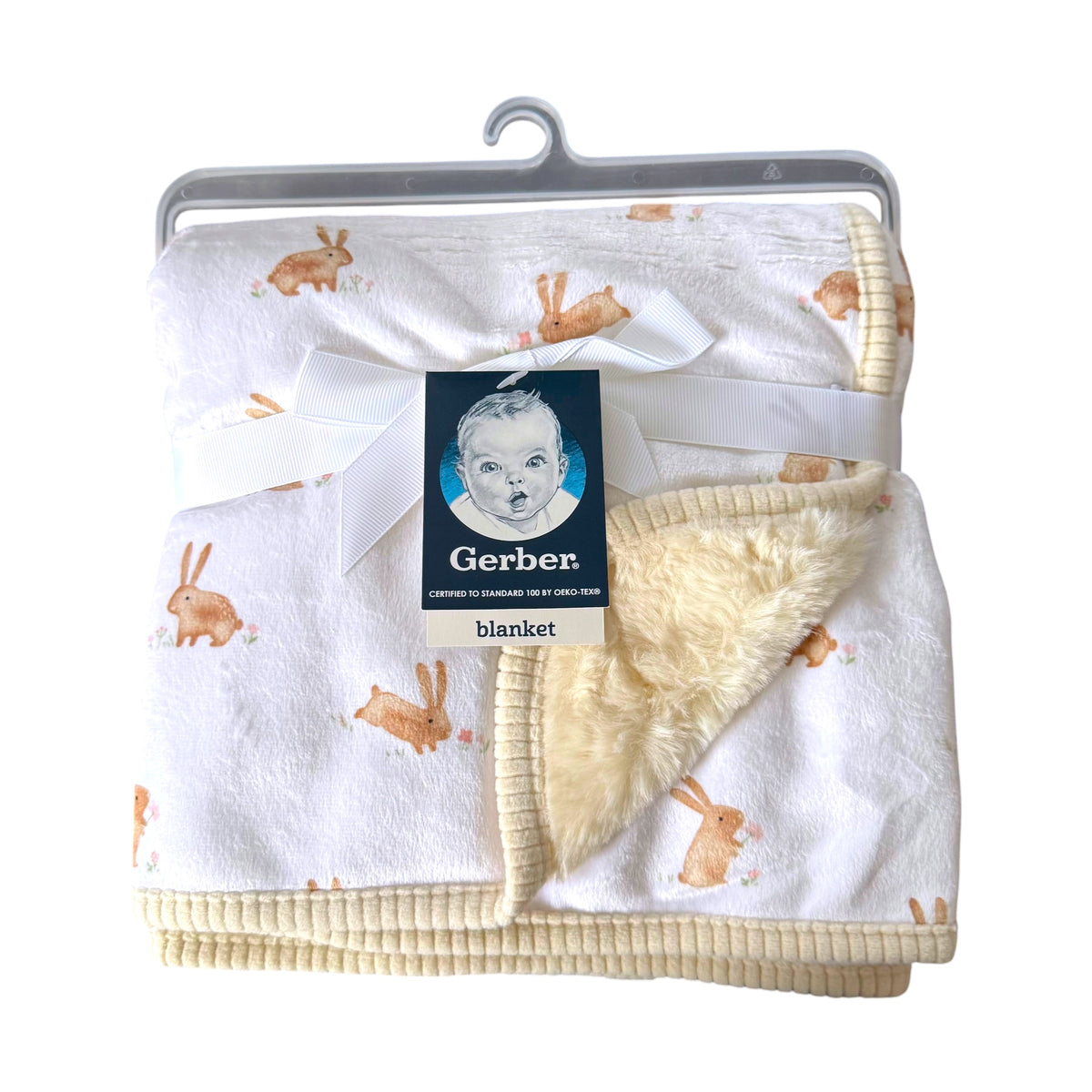 A Gerber baby blanket with a white plush exterior printed with light brown bunny motifs, featuring a soft cream sherpa lining and ribbed cream trim, packaged with a white ribbon and Gerber tag on a hanger.