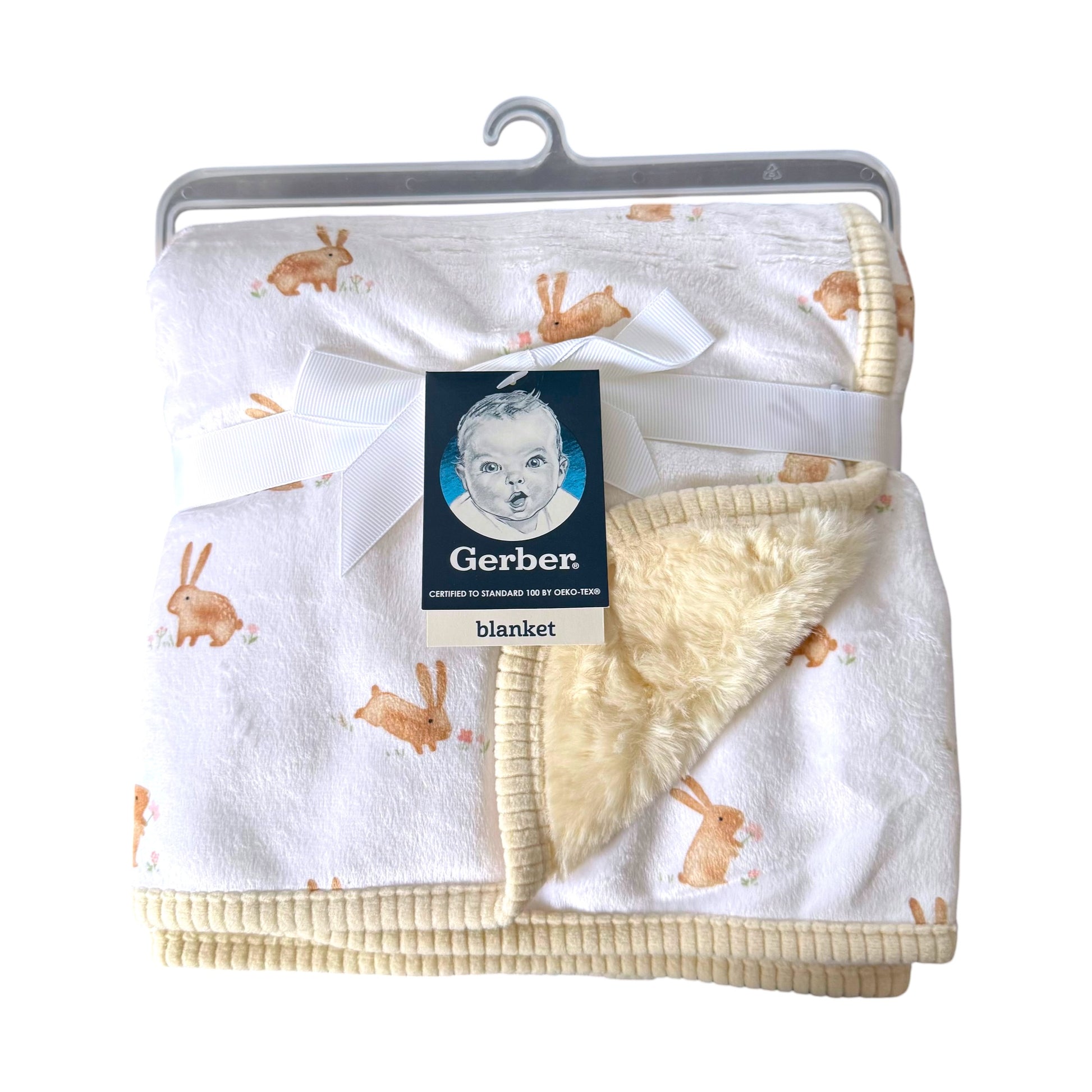 A Gerber baby blanket with a white plush exterior printed with light brown bunny motifs, featuring a soft cream sherpa lining and ribbed cream trim, packaged with a white ribbon and Gerber tag on a hanger.
