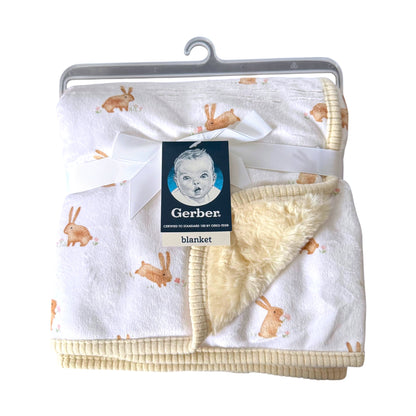 A Gerber baby blanket with a white plush exterior printed with light brown bunny motifs, featuring a soft cream sherpa lining and ribbed cream trim, packaged with a white ribbon and Gerber tag on a hanger.