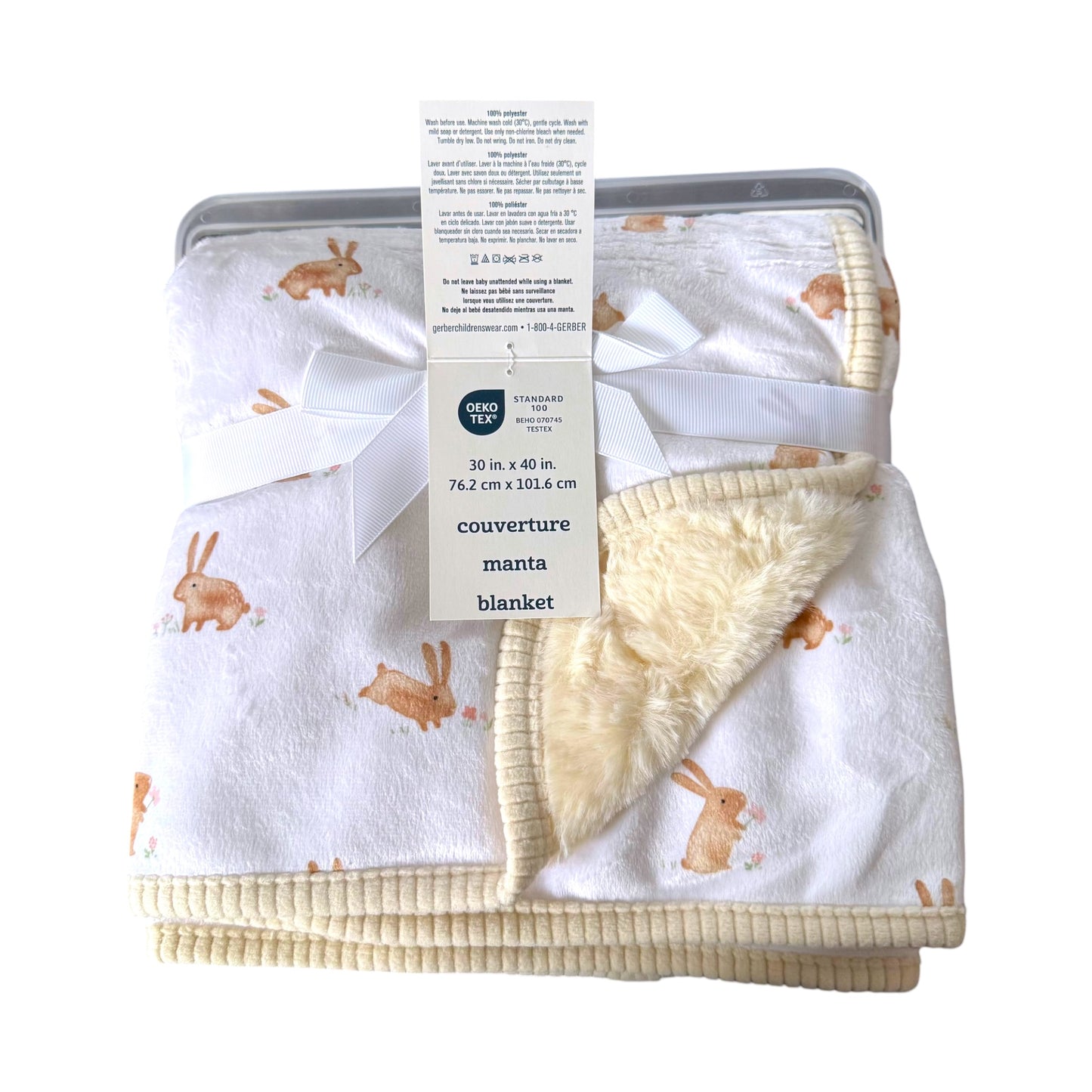 A folded baby blanket with a white sherpa fleece lining and a cream ribbed cotton cover, printed with a brown bunny pattern. The blanket is tied with a white ribbon and a paper tag from the brand Gerber