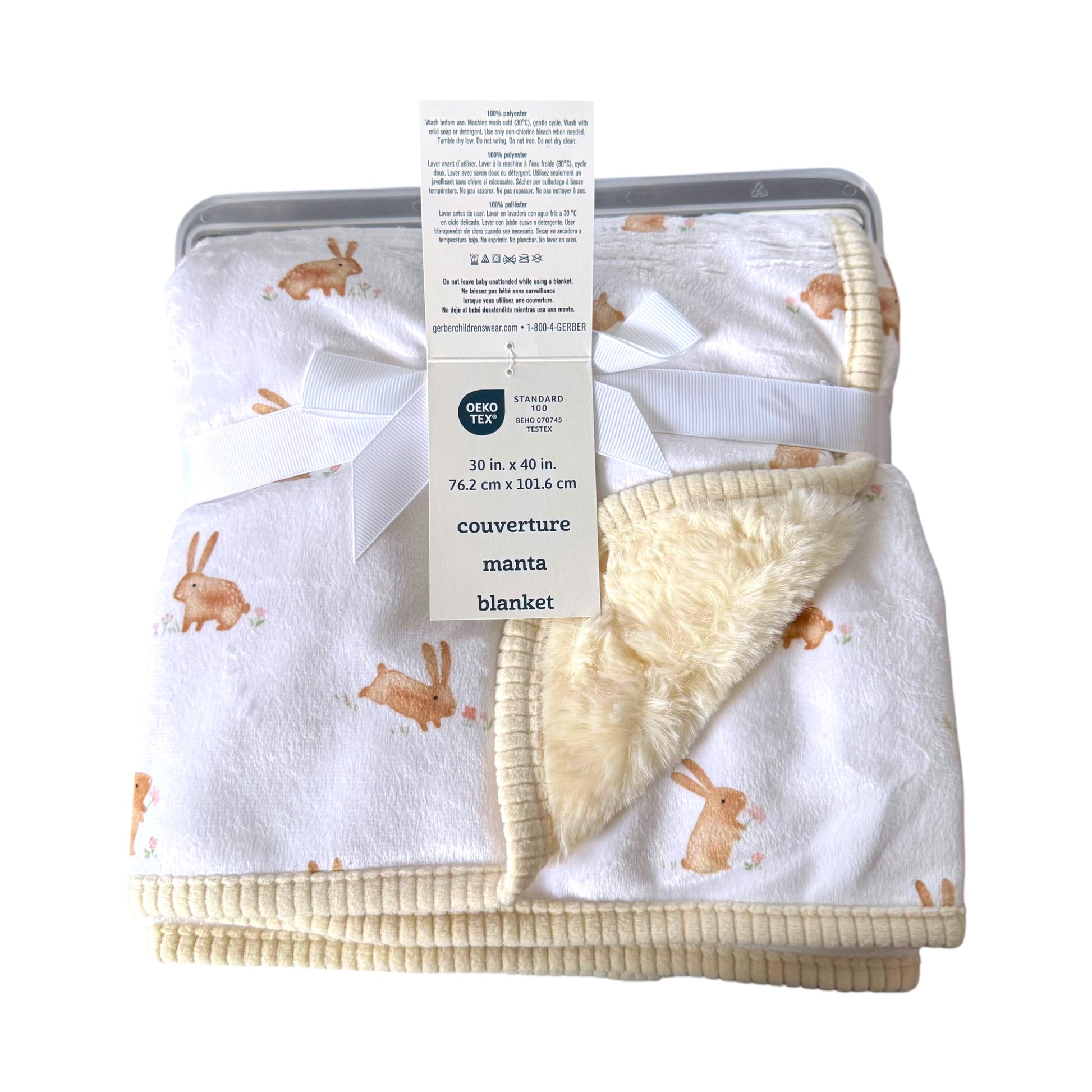 A folded baby blanket with a white sherpa fleece lining and a cream ribbed cotton cover, printed with a brown bunny pattern. The blanket is tied with a white ribbon and a paper tag from the brand Gerber