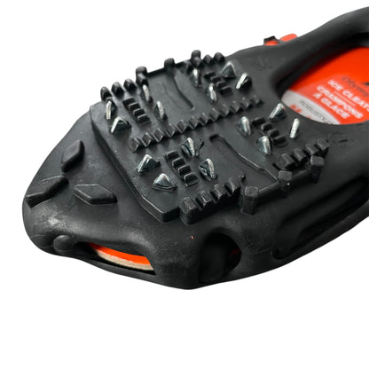 Closeup view of a pair of Olympia black ice cleats with orange branding on a white background