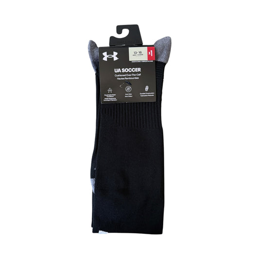 A pack of Under Armour soccer socks in black with gray cuffs, shown in their original retail packaging on a white background.