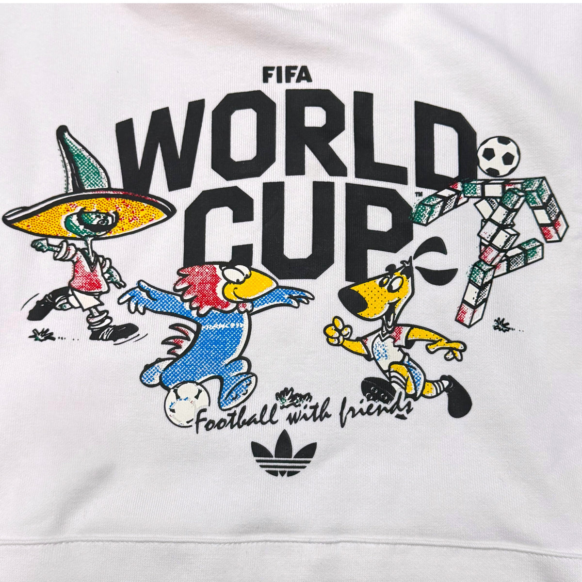 White sweatshirt featuring a colorful FIFA World Cup graphic with cartoon soccer players and the Adidas trefoil logo.