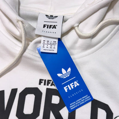 Close-up of a white Adidas x FIFA Classics hoodie showing the neck label, blue hangtag, and part of the black printed 'FIFA WORLD' text on the chest.