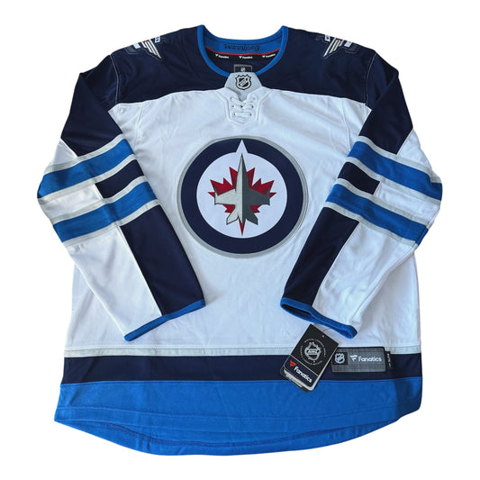 A Winnipeg Jets hockey jersey in white, navy, and blue, featuring the team's circular logo on the chest and two brand tags near the hem.